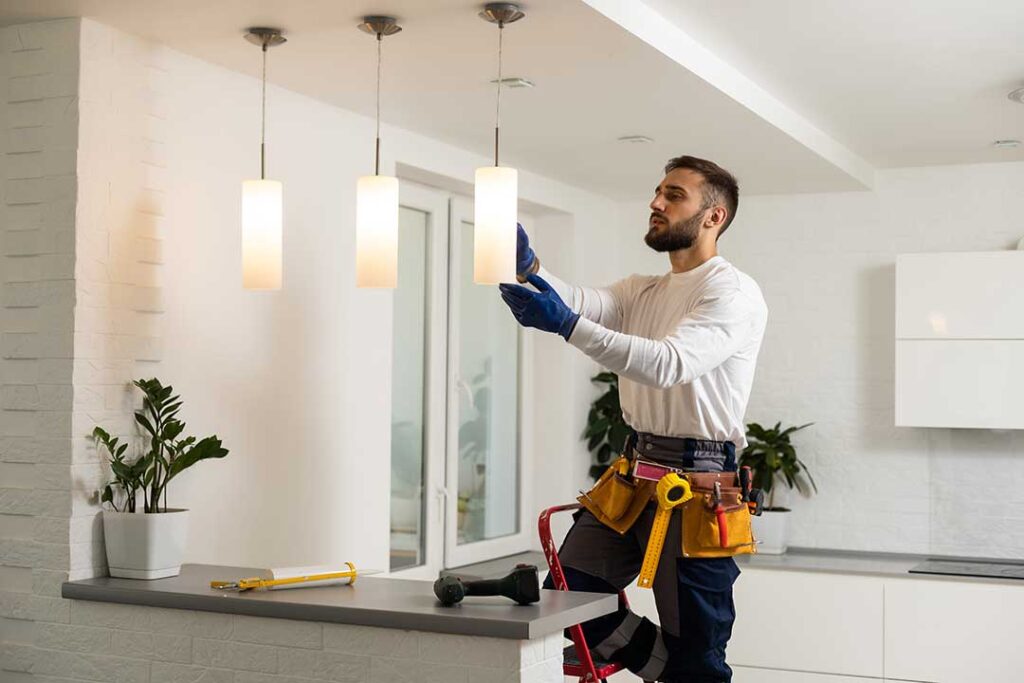 A person adjusting a home thermostat while sunlight comes through a nearby window.