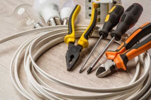 A hand plugging multiple electronics into a single wall outlet with visible power strips and extension cords.