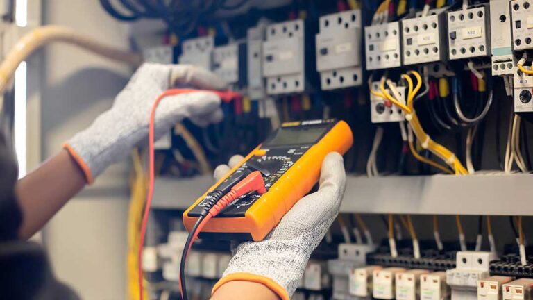An electrician checks a wall outlet with a voltage tester in a residential living room.