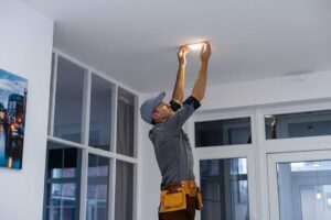 An electrical inspector examining a home's circuit breaker panel with a flashlight.
