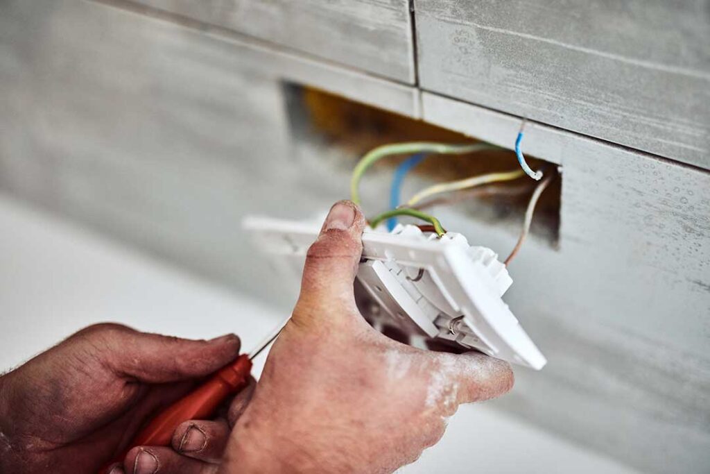Person pressing the test button on a ceiling-mounted smoke detector inside a home.